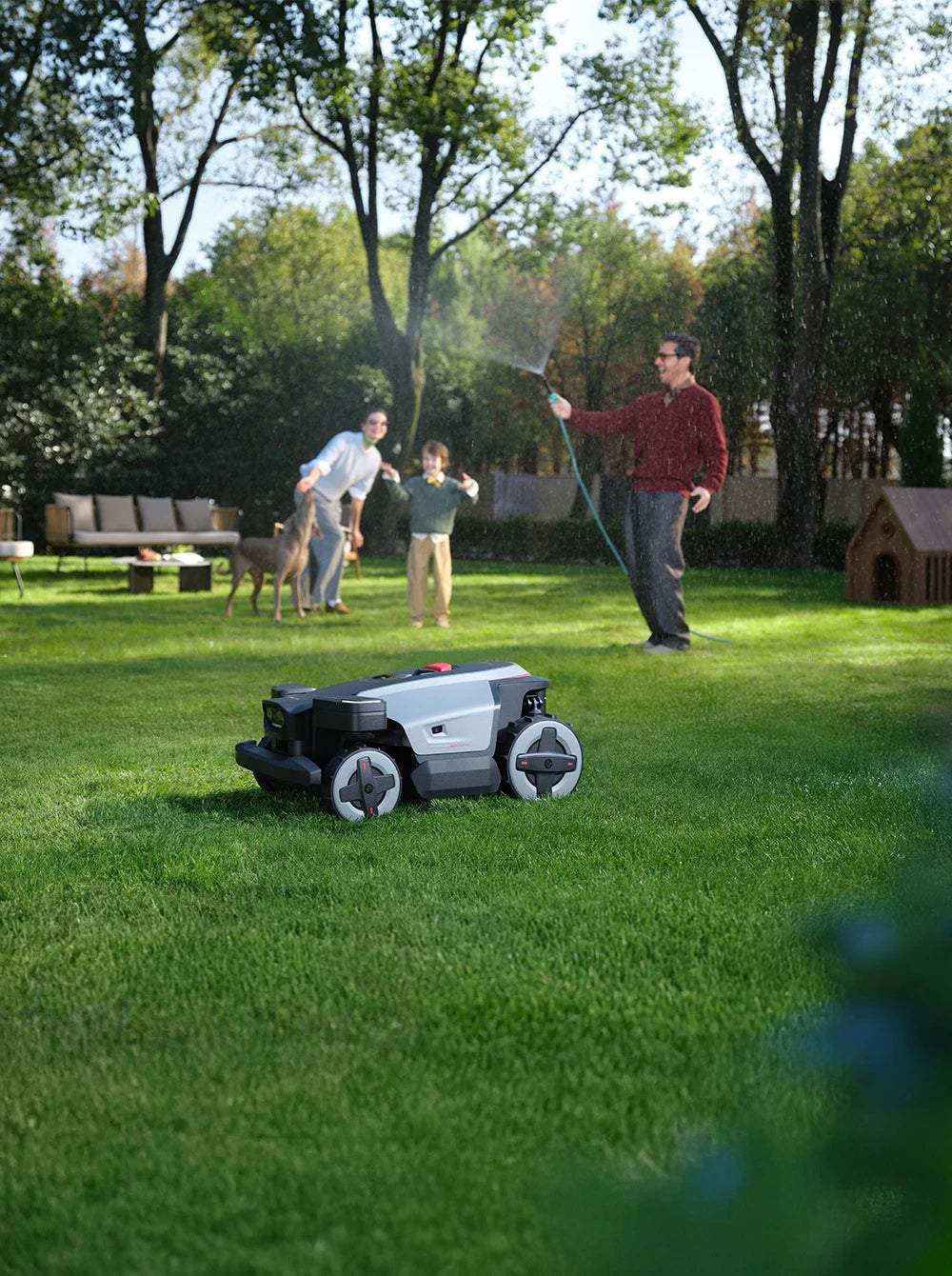 Robotic lawn mower on a grassy lawn with people and pets in the background