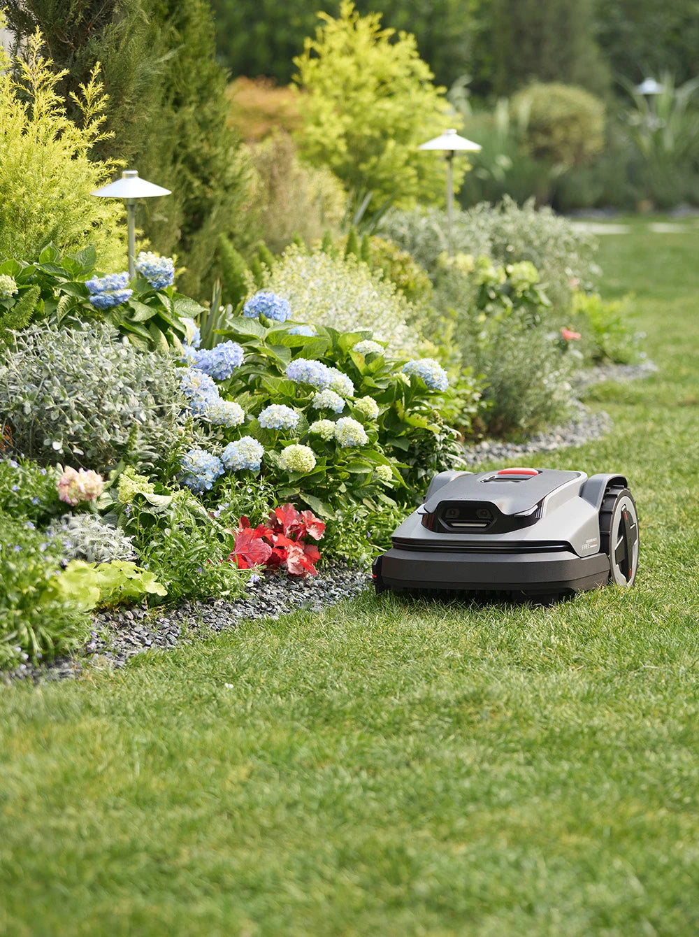 Robotic lawn mower in a garden with flowers and greenery