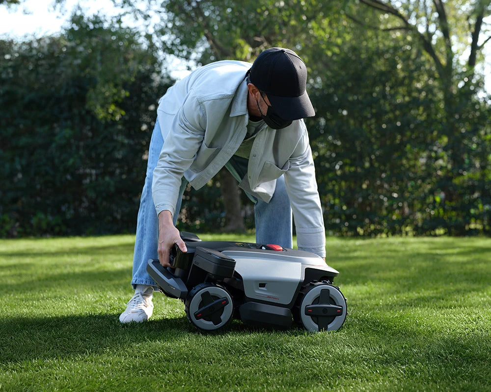 Person lifting a RockMow Z1 robot mower from the lawn, illustrating its anti-theft protection.