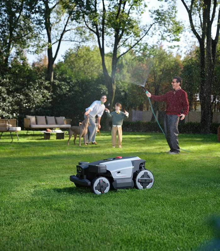 RockMow Z1 robotic lawn mower cutting a family garden while people and a dog relax nearby.