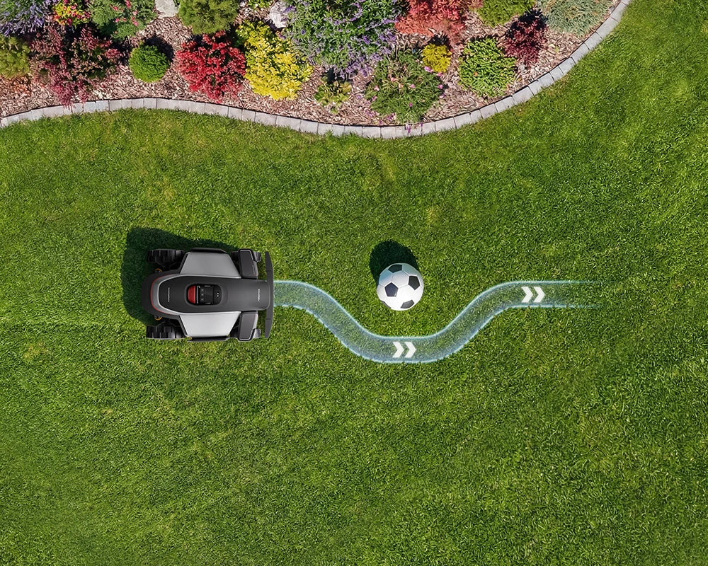 Top-down view of a robotic lawn mower on a green lawn, with a soccer ball graphic and a light blue curved path indicating navigation or coverage.