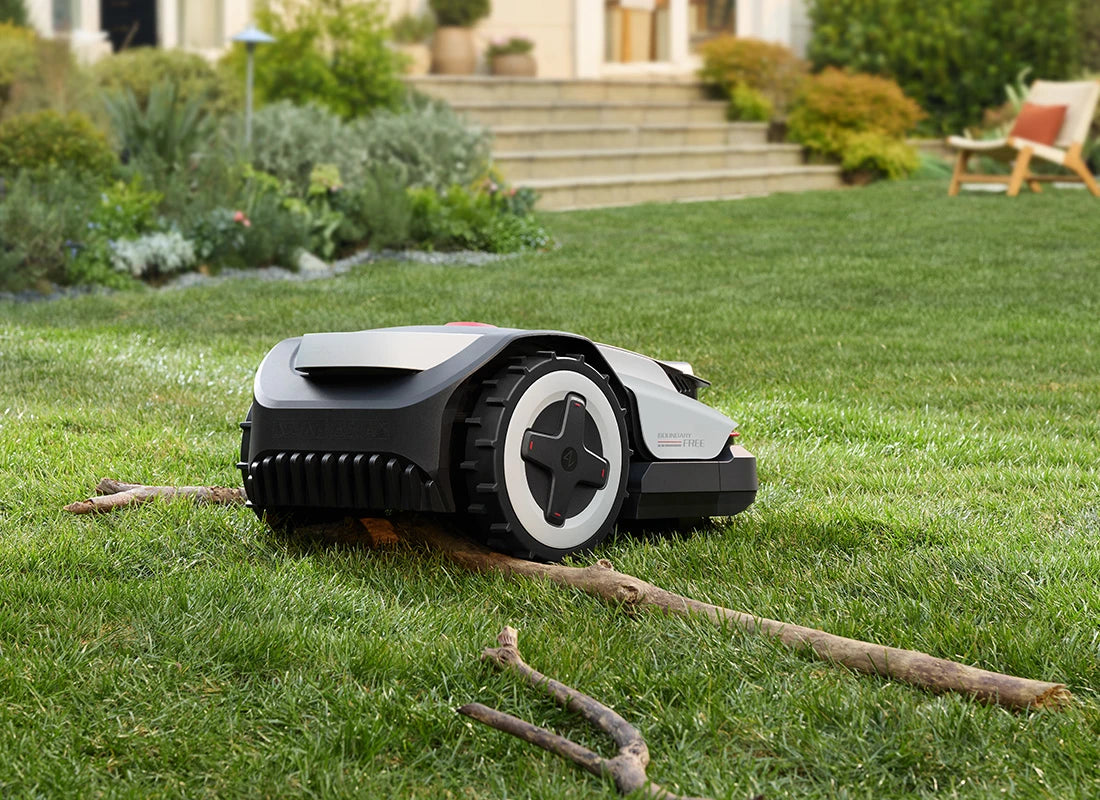 RockNeo Q1 robotic lawn mower driving over branches on a garden lawn