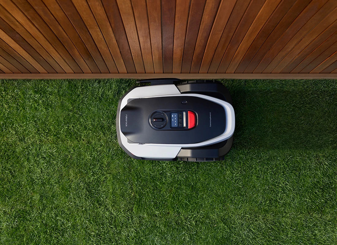 RockNeo Q1 robotic lawn mower cutting close to a wooden garden boundary