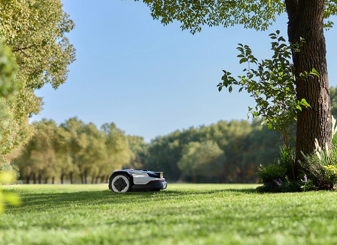 Robotic lawn mower on a grassy lawn with trees in the background